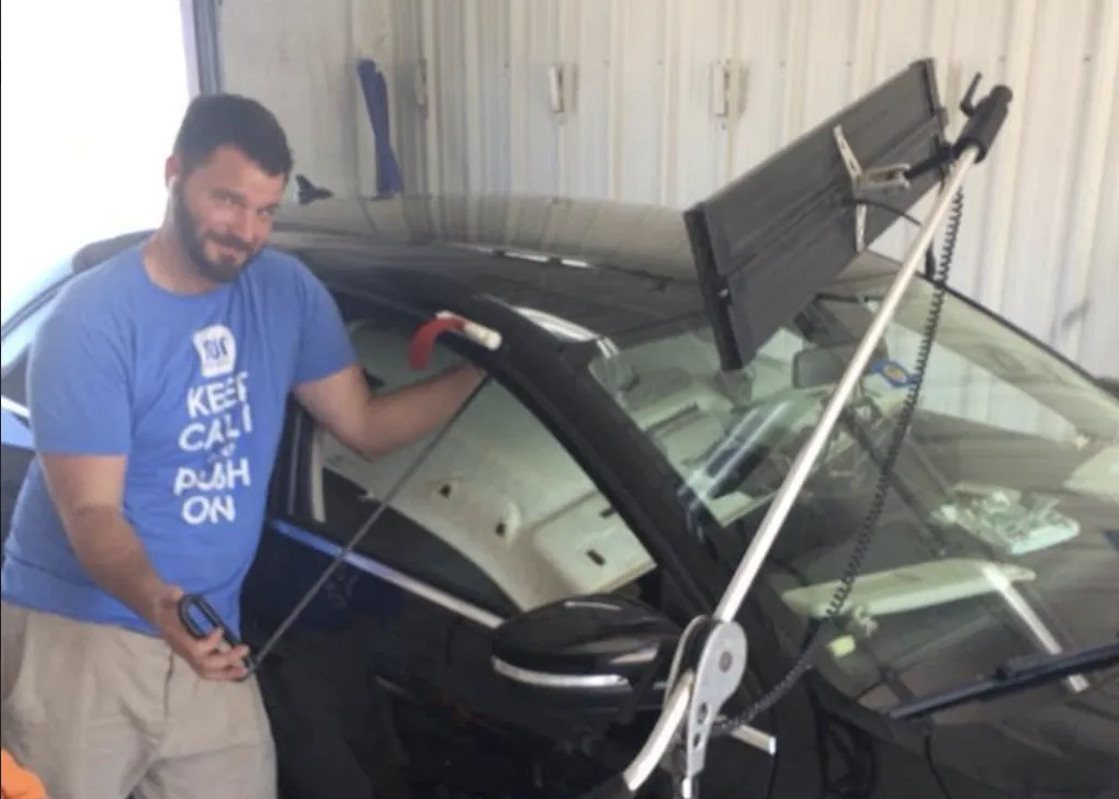 Technician using a paintless dent repair rod on a black car at Star Auto Body